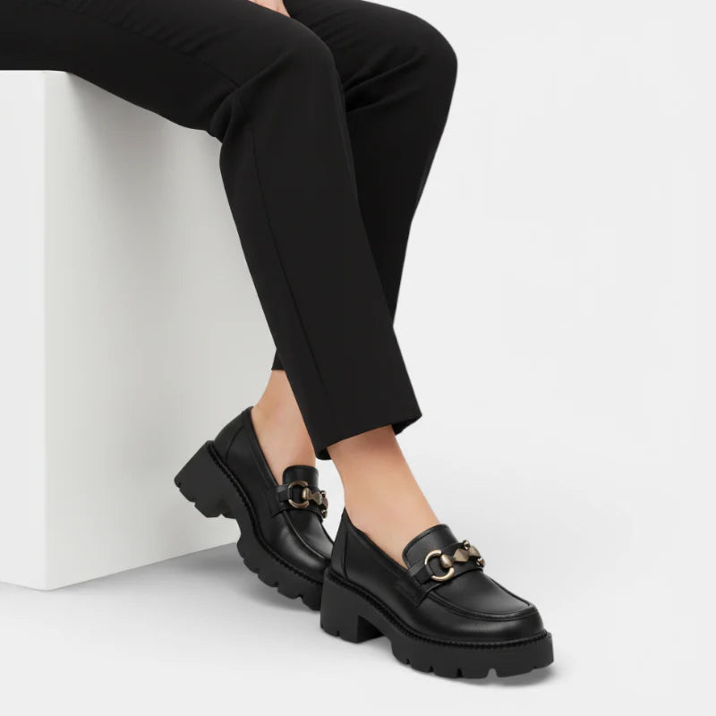 Femme assise portant des mocassins plateforme en cuir mat noir avec chaînette argentée